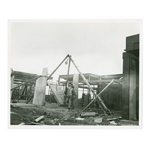 R.M. Schindler, architect, black and white photograph of Schindler House under construction with two men are shown hoisting a poured concrete slab into place using a pulley system on the partially completed house. 
