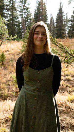 Gallery assistant in green and black dress, standing in a forest landscape background